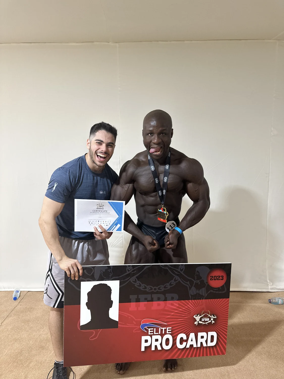 Emad Deznabi with his athlete and the IFBB Elite Pro Card board, 2023